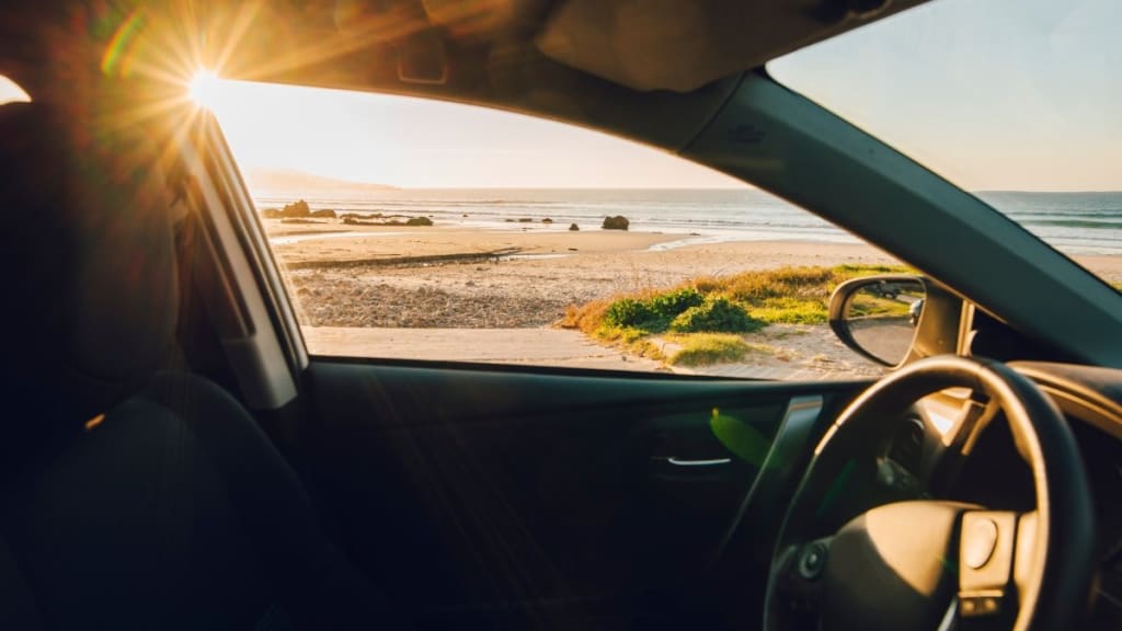 The driver's seat of a car looking out at the beach.